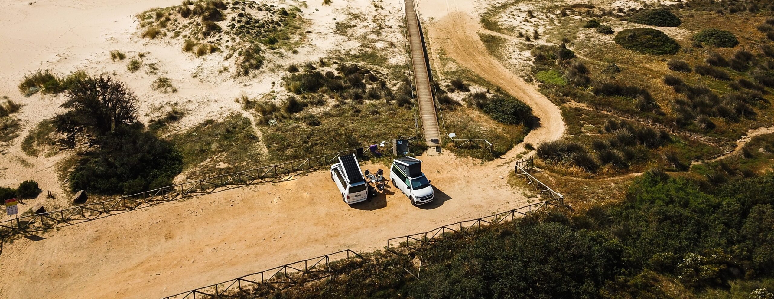 VW California Beach und Ocean auf sandigem Platz an der potugisischen Küste aus Vogelperspektive.