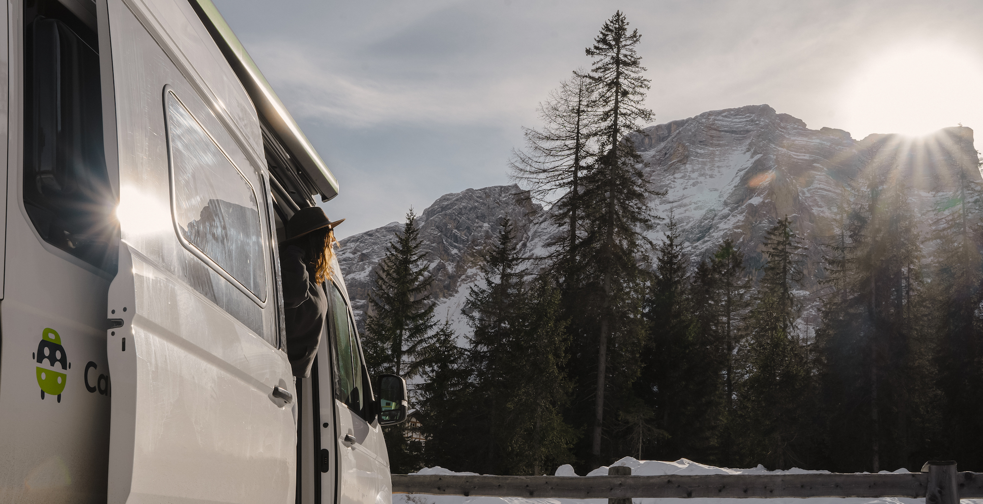 Frau schaut aus VW Grand California Campervan vor Bergen im Schnee