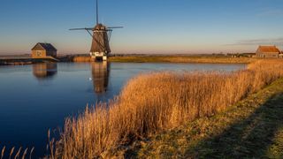 Vom Sonnenlicht angestrahlte Windmühle in Kinderdijk von der anderen Seite des Fluss aus fotografiert: ein tolles Ausflugsziel beim Camping in Holland am Meer