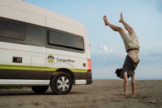 Mann macht einen Handstand neben einem CamperBoys Camper in Holland am Sandstrand