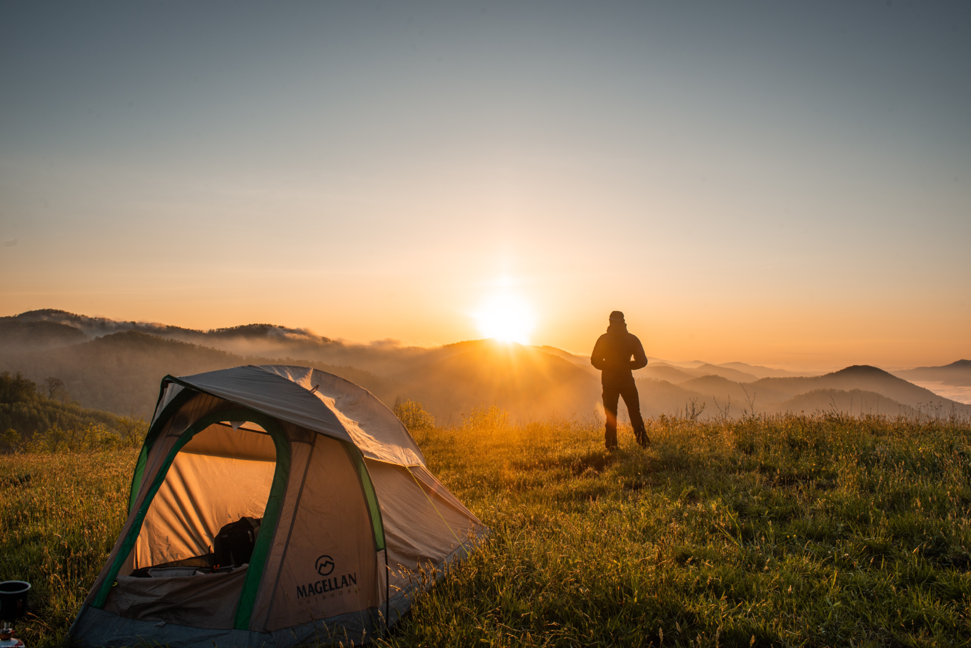 Mann bei Sonnenaufgang vor seinem Zelt beim wildcampen