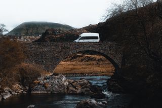 Ein VW Grand California überquert einen Fluss mithilfe einer Brücke.
