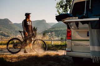 Ein Mountainbiker steht neben einem CamperBoys Camper und blickt in die umliegenden Berge. 