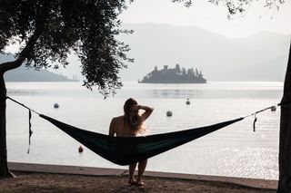 Eine Frau sitzt am Ufer des Lago Maggiore in einer Hängematte und blickt auf eine Insel.