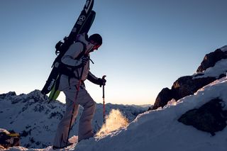 Ein Mann in und mit Skiausrüstung besteigt einen Berg.