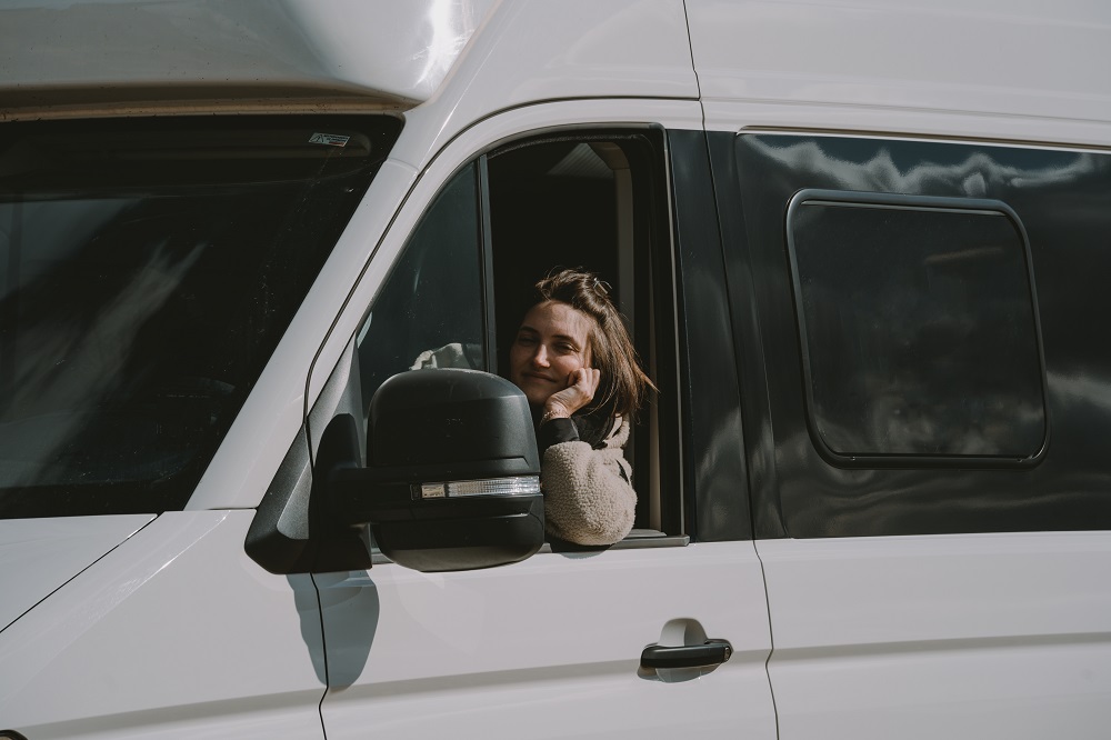 Eine Frau sitzt am Steuer eines VW Grand California Campers. Das Fenster ist offen und sie lächelt.