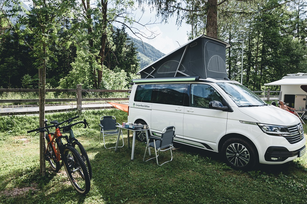 VW Ocean mit aufgestelltem Dachzelt auf einem Campingplatz im Wald inklusive Mountainbikes 