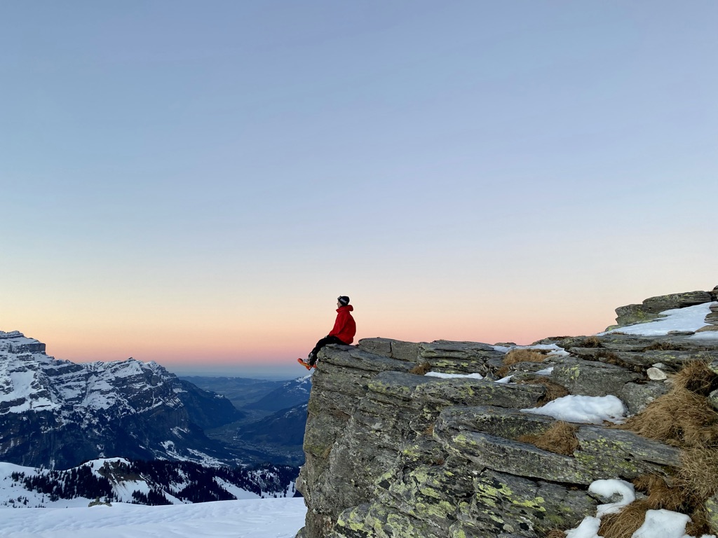 Wanderer sitzt auf Felsvorsprung in verschneiten Bergen
