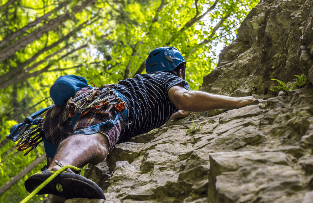 Mann in kompletter Kletterausrüstung klettert eine steile Felswand empor