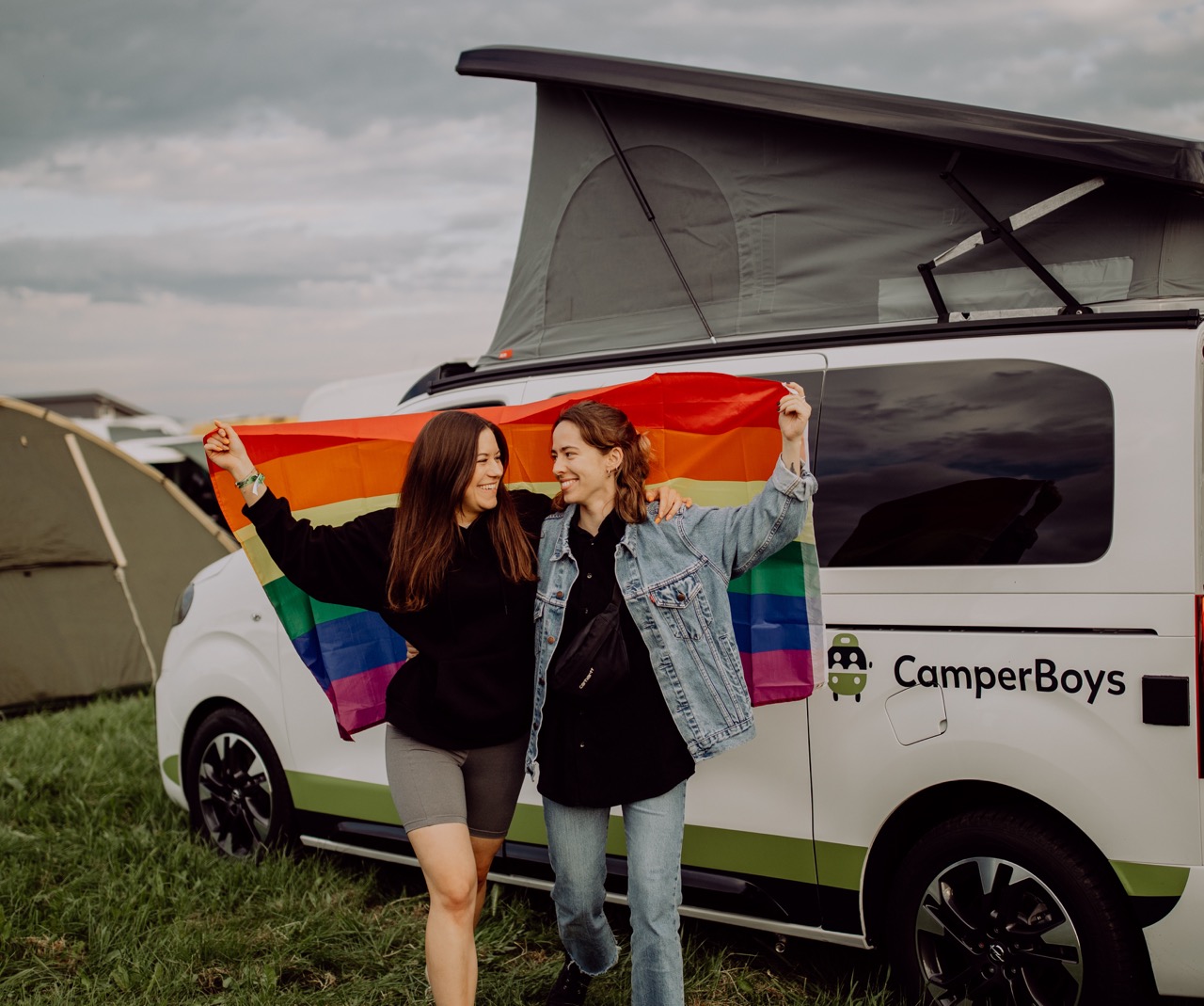 Zwei Frauen mit LGBTQ+ Flagge vor Opel Crosscamp