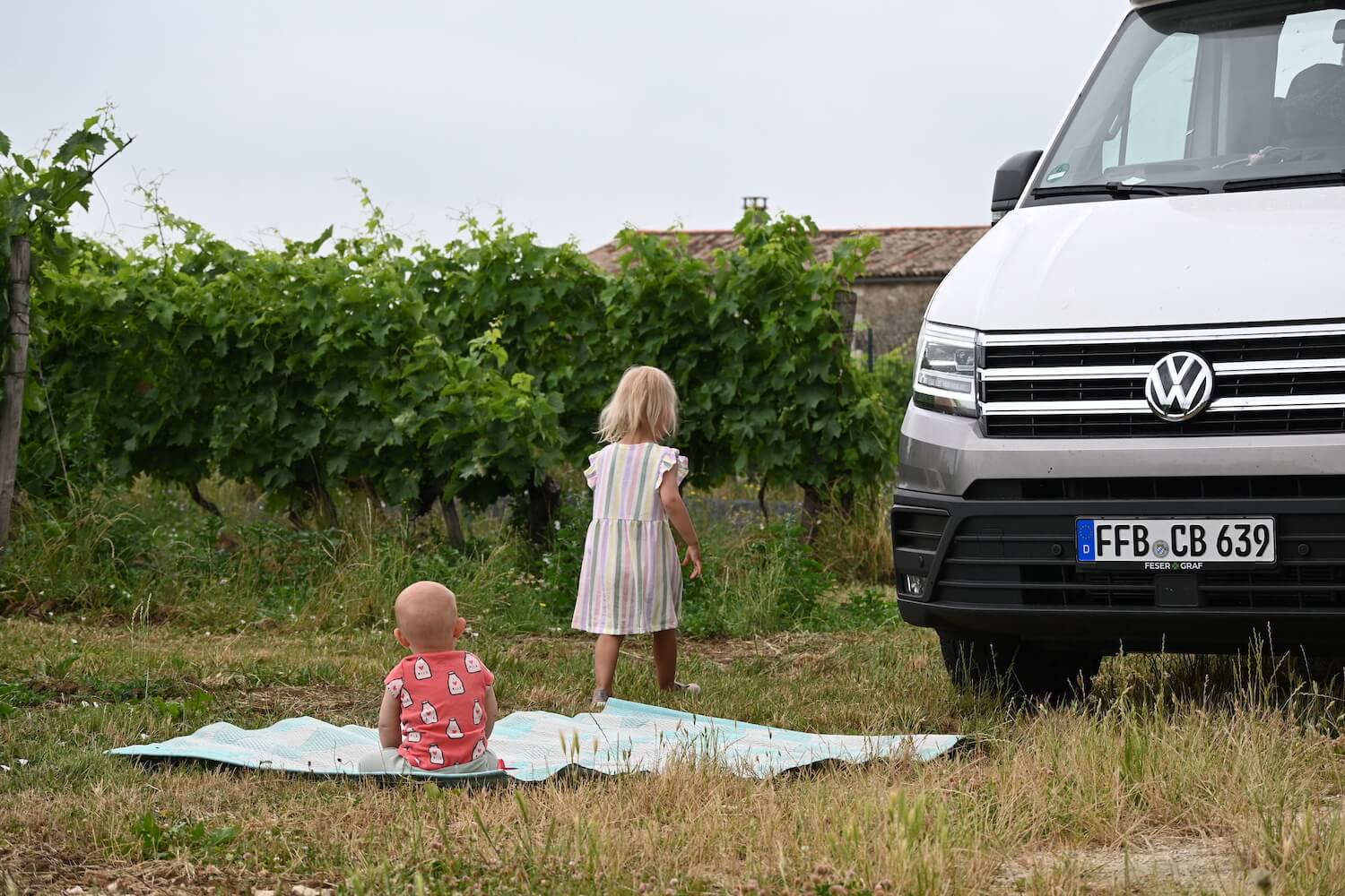 Reisen mit Kind: Baby und Kleinkind beim spielen auf der Wiese vor VW Grand California Camper 