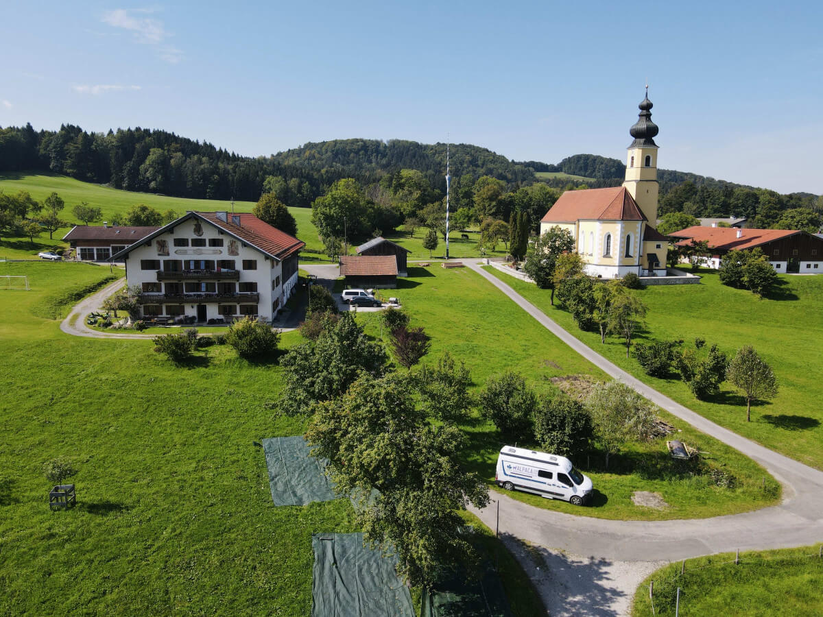 Luftaufnahme von einem Bauernhof und einer Kirche in einem kleinen Dorf mit geparktem Camper.