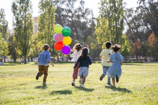 Kinder rennen auf Wiese mit Luftballons