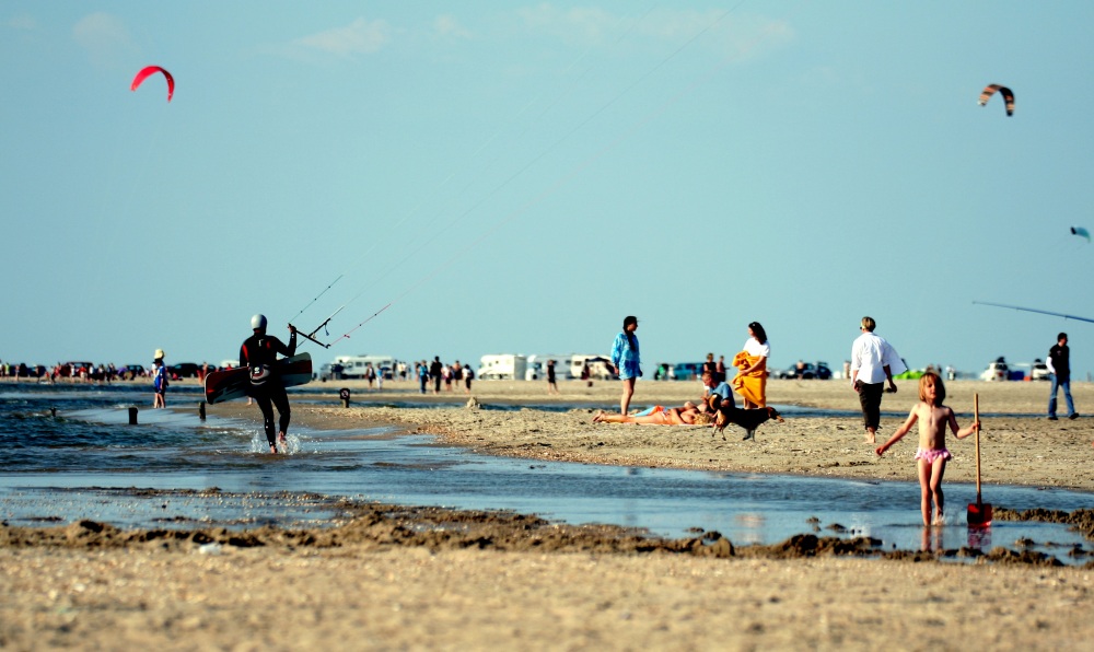 Strand mit spielenden Kindern, Kitern und anderen Personen. 
