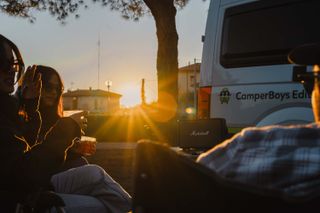 Eine Freundesgruppe sitzt bei Sonnenuntergang vor einem Camper.