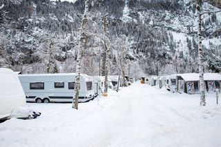 Ein verschneiter Campingplatz mit einigen Vans vor einer Bergkulisse.